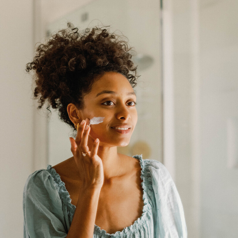 woman applying moisturizer skincare in the mirror.