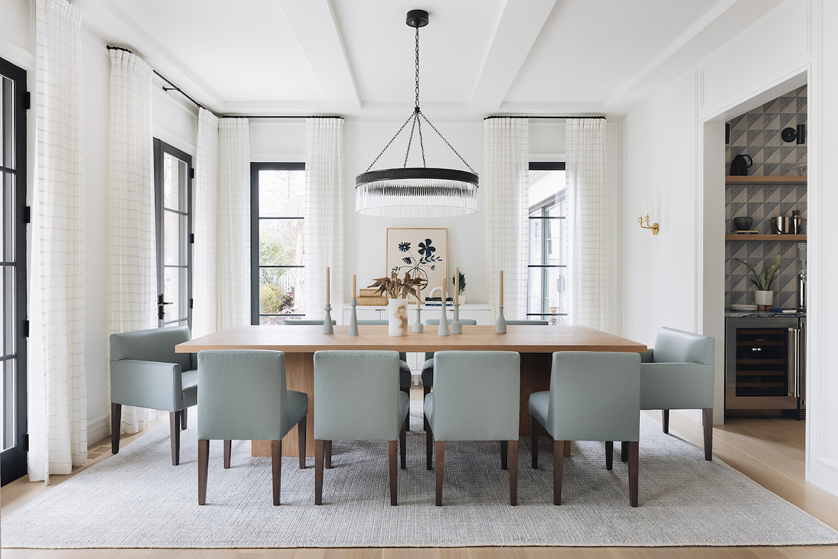 Modern white dining room with long rectangular table surrounded by light blue tufted chairs.