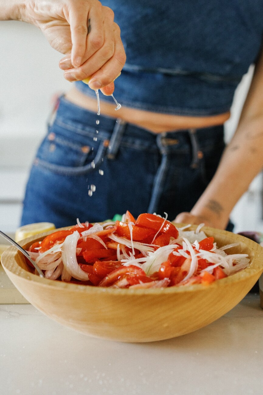 Tomato salad with onion, being drizzled with lemon juice